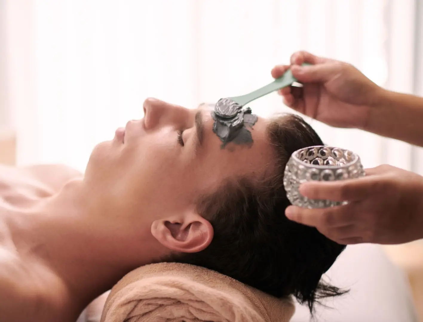 Man receiving a facial clay mask treatment.