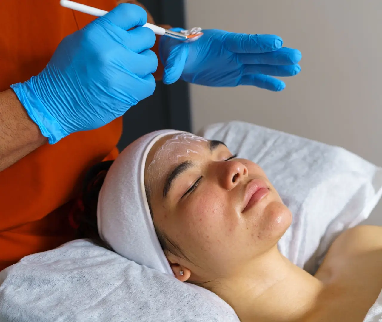 Woman receiving facial treatment with blue gloves.