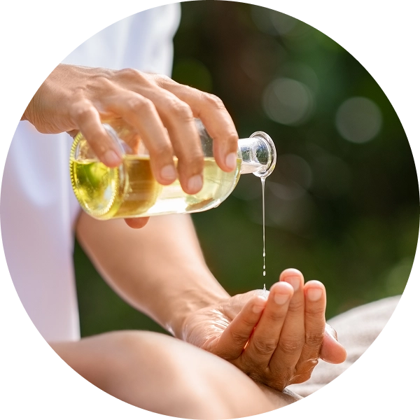 Hand pouring oil from glass bottle outdoors.